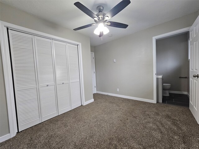 unfurnished bedroom with ensuite bathroom, a closet, dark colored carpet, and ceiling fan