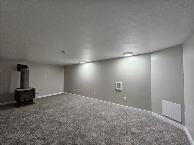 basement featuring carpet flooring, a wood stove, and a textured ceiling