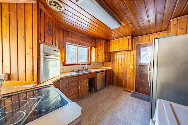 kitchen with sink, wood walls, wood ceiling, appliances with stainless steel finishes, and decorative backsplash