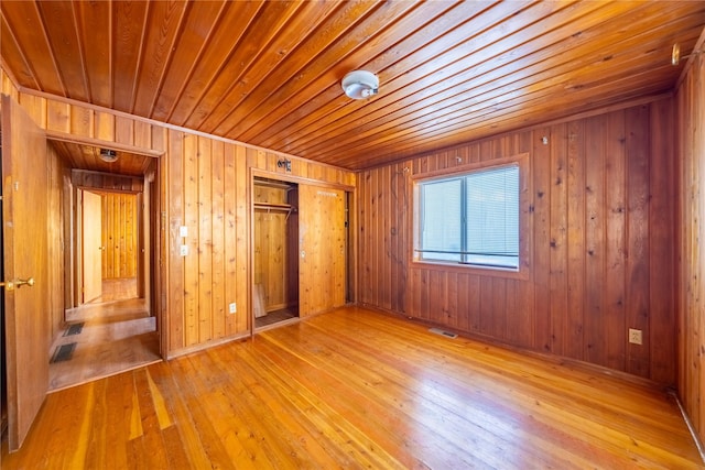 unfurnished bedroom featuring light hardwood / wood-style floors, a closet, and wood walls