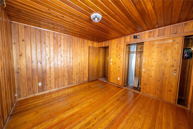 unfurnished bedroom with hardwood / wood-style floors, a closet, and wood walls