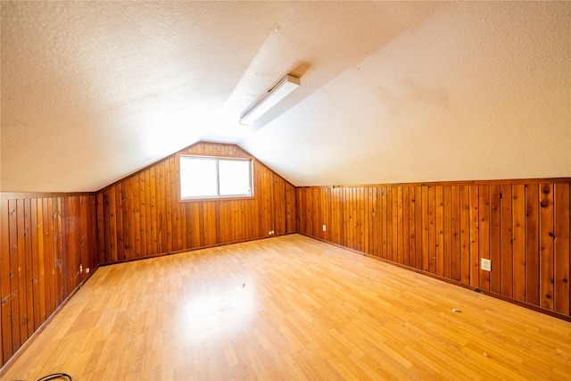 additional living space featuring hardwood / wood-style flooring, vaulted ceiling, and a textured ceiling