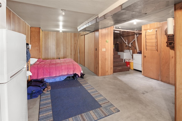 bedroom with wood walls, white fridge, and washing machine and clothes dryer