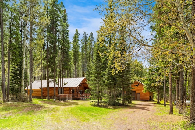 log-style house with a wooden deck, dirt driveway, a front yard, a view of trees, and metal roof