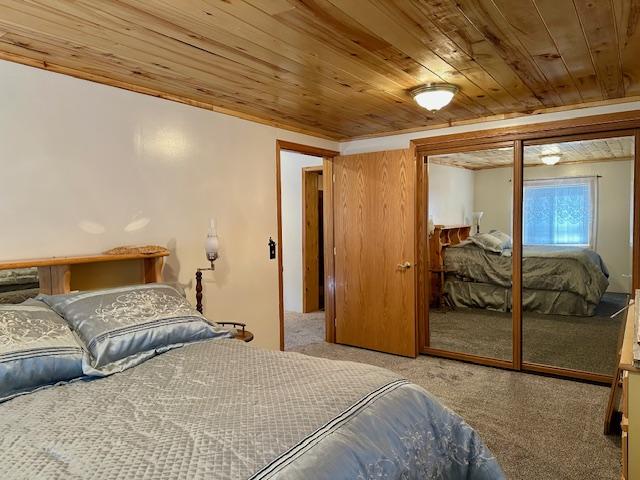 bedroom with carpet flooring, wooden ceiling, and a closet