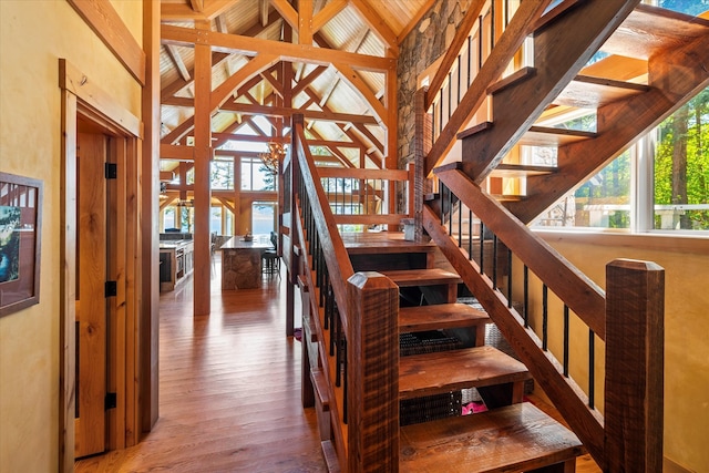 stairs featuring high vaulted ceiling, beamed ceiling, and hardwood / wood-style floors
