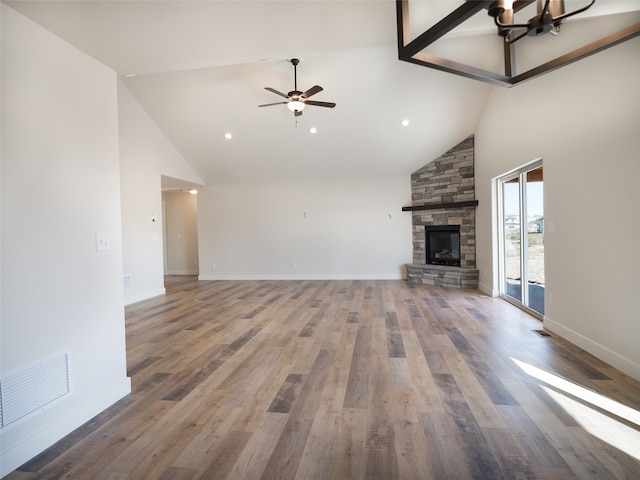 unfurnished living room with ceiling fan with notable chandelier, a fireplace, hardwood / wood-style floors, and high vaulted ceiling