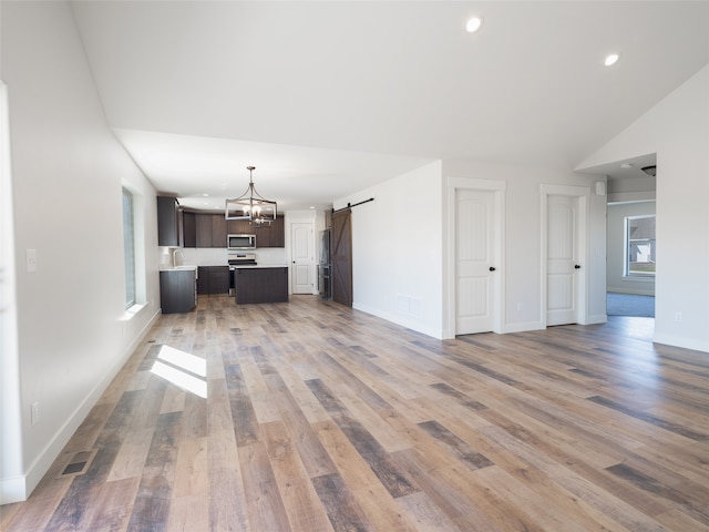 unfurnished living room with wood-type flooring, lofted ceiling, sink, and a barn door