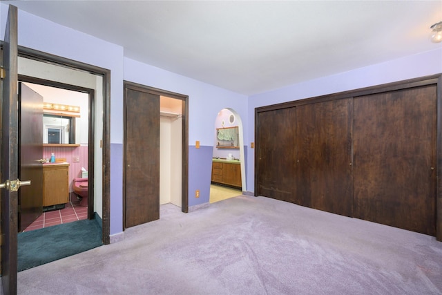 unfurnished bedroom with ensuite bathroom and light colored carpet