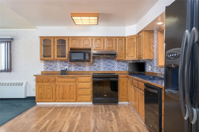 kitchen featuring sink, radiator, light hardwood / wood-style floors, decorative backsplash, and black appliances