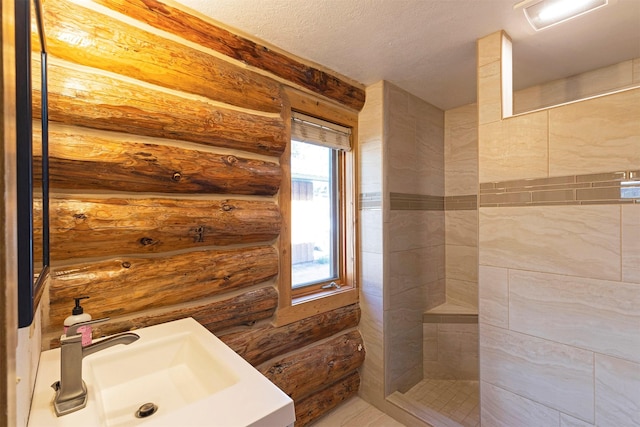 bathroom featuring a textured ceiling, a tile shower, and sink