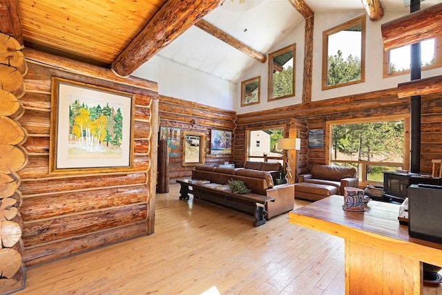 living room featuring a healthy amount of sunlight, a wood stove, rustic walls, and high vaulted ceiling