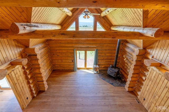 unfurnished living room featuring beam ceiling, a wood stove, ceiling fan, and light hardwood / wood-style flooring