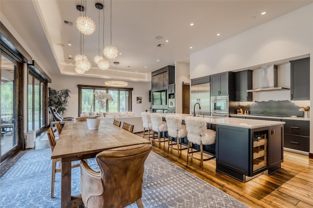 dining room featuring an inviting chandelier, beverage cooler, light hardwood / wood-style floors, and a raised ceiling