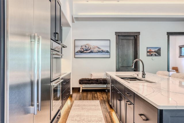 kitchen featuring a center island, sink, appliances with stainless steel finishes, dark hardwood / wood-style flooring, and light stone counters