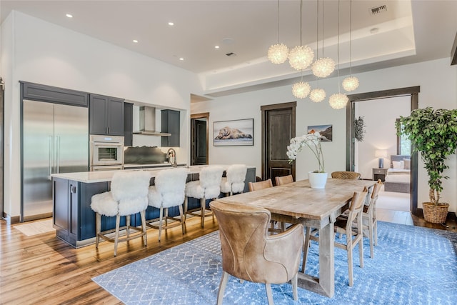 dining area featuring sink, a raised ceiling, and light wood-type flooring