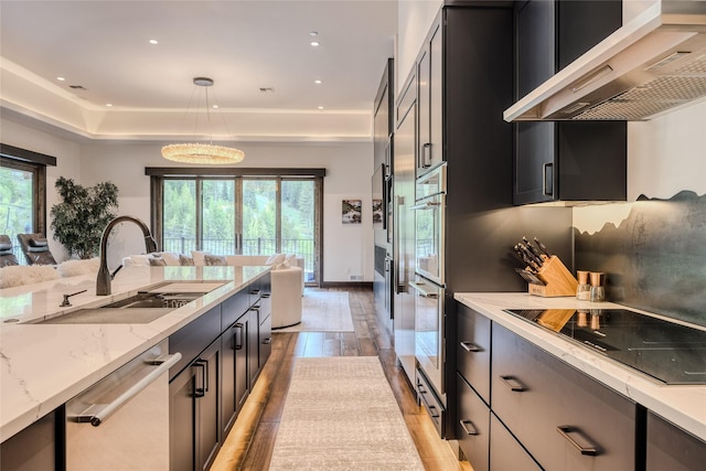 kitchen featuring black electric stovetop, decorative light fixtures, dishwasher, wall chimney range hood, and sink