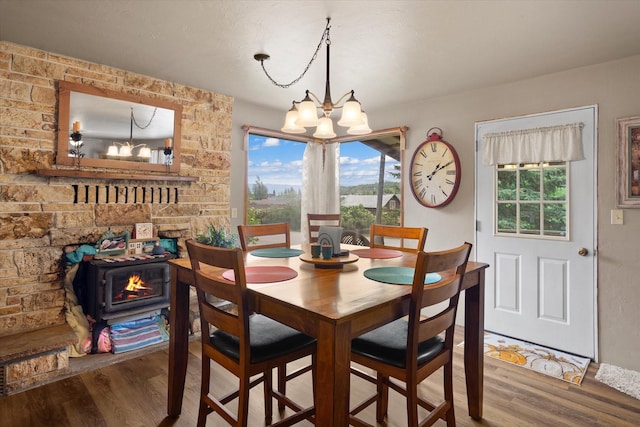 dining room with a wood stove, hardwood / wood-style floors, a healthy amount of sunlight, and an inviting chandelier