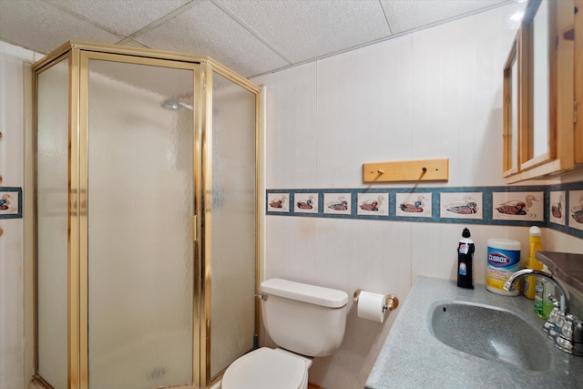 bathroom with a drop ceiling, toilet, a shower with door, and vanity