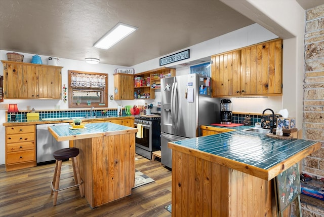 kitchen with a kitchen bar, appliances with stainless steel finishes, dark hardwood / wood-style flooring, sink, and tile counters