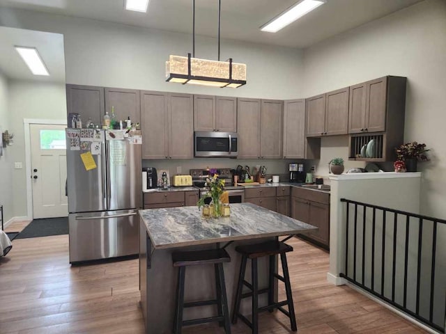 kitchen featuring hanging light fixtures, stainless steel appliances, a breakfast bar, a kitchen island, and light wood-type flooring