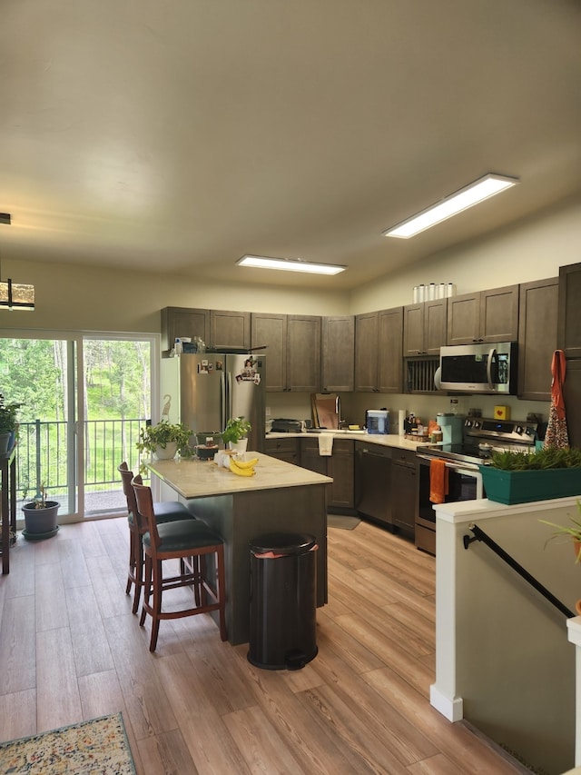 kitchen featuring light wood-type flooring, a breakfast bar, dark brown cabinetry, stainless steel appliances, and a center island