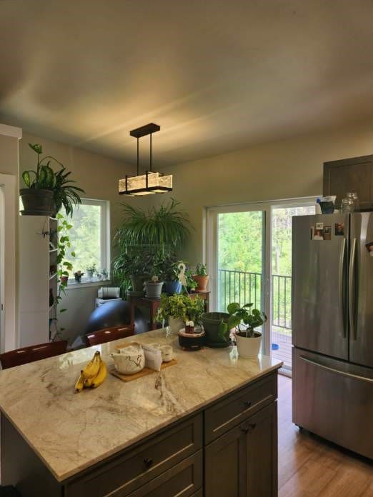 kitchen with stainless steel fridge, light stone counters, decorative light fixtures, light hardwood / wood-style flooring, and a center island