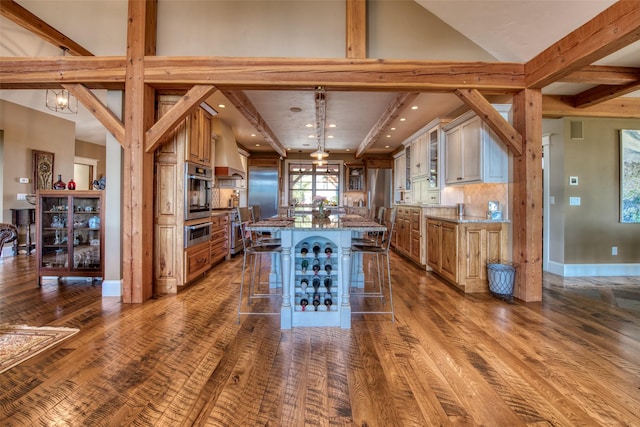 kitchen featuring a large island, a breakfast bar area, premium range hood, hardwood / wood-style floors, and light stone counters