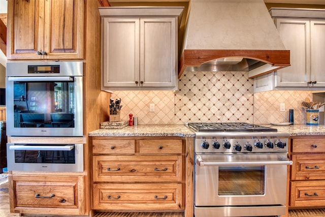 kitchen with tasteful backsplash, light stone countertops, custom range hood, and appliances with stainless steel finishes