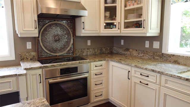 38648 Masumola Rd, Polson, MT 59860 - kitchen featuring oven, black electric stovetop, cream cabinetry, wall chimney range hood, and light stone countertops