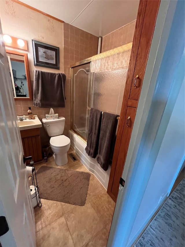 full bathroom with vanity, shower / bath combination with glass door, tile walls, tile patterned flooring, and toilet