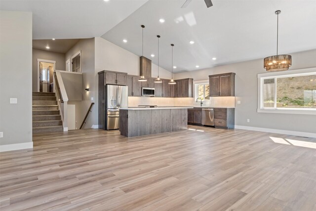 kitchen with a spacious island, stainless steel appliances, hanging light fixtures, and light hardwood / wood-style flooring