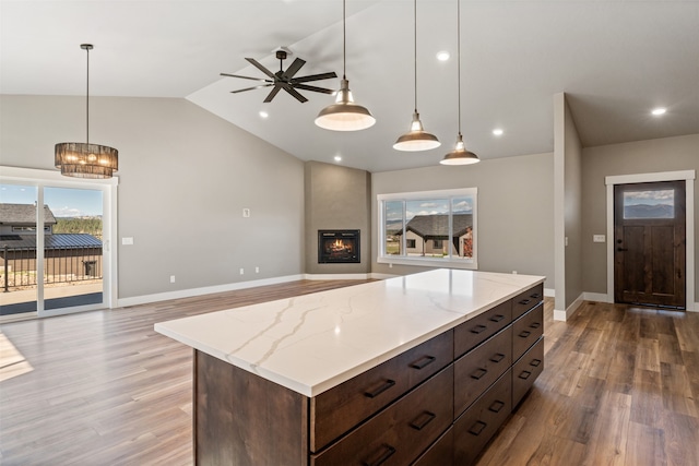 kitchen featuring ceiling fan with notable chandelier, a fireplace, pendant lighting, light wood-type flooring, and lofted ceiling