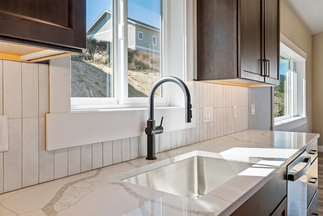 interior space featuring a healthy amount of sunlight, dark brown cabinetry, sink, and light stone counters