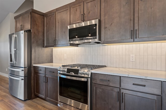 kitchen with light stone counters, dark brown cabinetry, lofted ceiling, appliances with stainless steel finishes, and light hardwood / wood-style floors