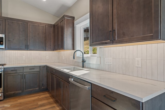 kitchen with sink, dark wood-type flooring, appliances with stainless steel finishes, light stone countertops, and vaulted ceiling