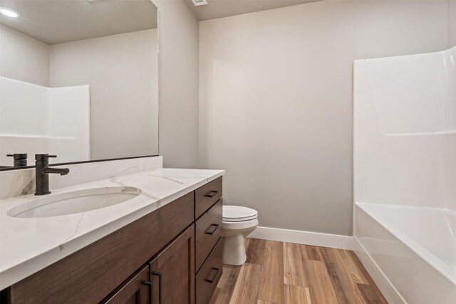 bathroom featuring a washtub, wood-type flooring, vanity, and toilet