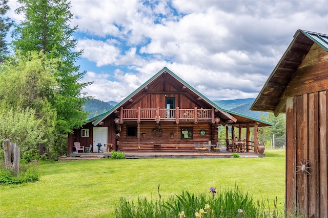 rear view of property featuring a mountain view, a balcony, and a yard