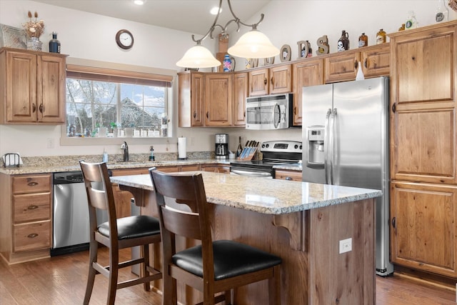 kitchen with dark wood finished floors, a kitchen island, light stone countertops, stainless steel appliances, and a sink