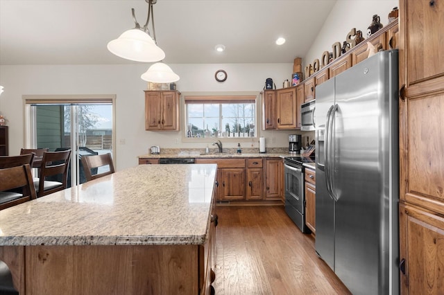 kitchen with stainless steel appliances, dark wood-type flooring, hanging light fixtures, a center island, and brown cabinetry