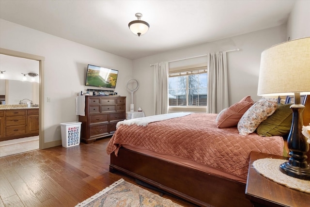 bedroom with ensuite bathroom, wood finished floors, and baseboards