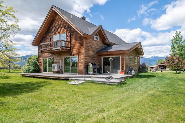 rear view of property featuring a deck with mountain view, a lawn, and a balcony