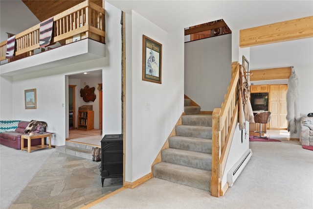 stairs with light colored carpet, a wood stove, and a baseboard heating unit