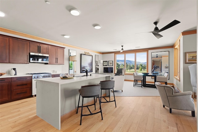 kitchen with light hardwood / wood-style flooring, a breakfast bar, stainless steel appliances, ornamental molding, and a center island with sink