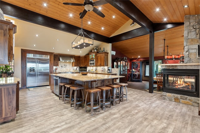 kitchen featuring beamed ceiling, built in refrigerator, hanging light fixtures, light stone countertops, and wall chimney exhaust hood