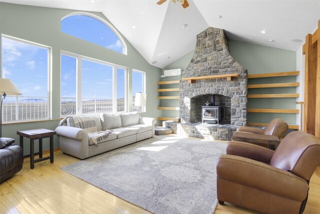 living room with a stone fireplace, light hardwood / wood-style floors, high vaulted ceiling, and ceiling fan