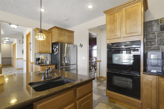 kitchen with dark stone counters, stainless steel fridge, decorative light fixtures, sink, and double oven