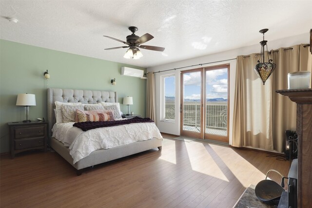 bedroom featuring a textured ceiling, access to outside, hardwood / wood-style floors, a wall mounted AC, and ceiling fan