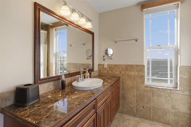 bathroom with tile flooring, a healthy amount of sunlight, vanity, and tile walls