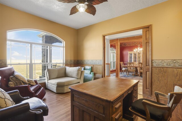 home office featuring a textured ceiling, wood-type flooring, and ceiling fan with notable chandelier